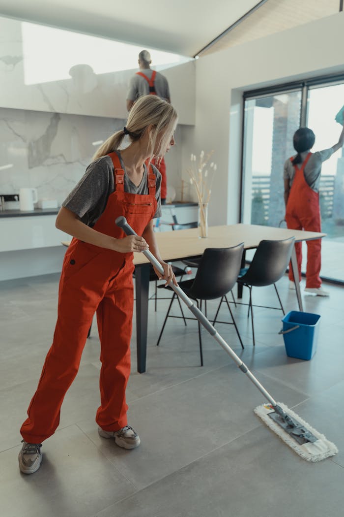 services-01 Cleaning team in red overalls mopping and sanitizing a modern home interior.